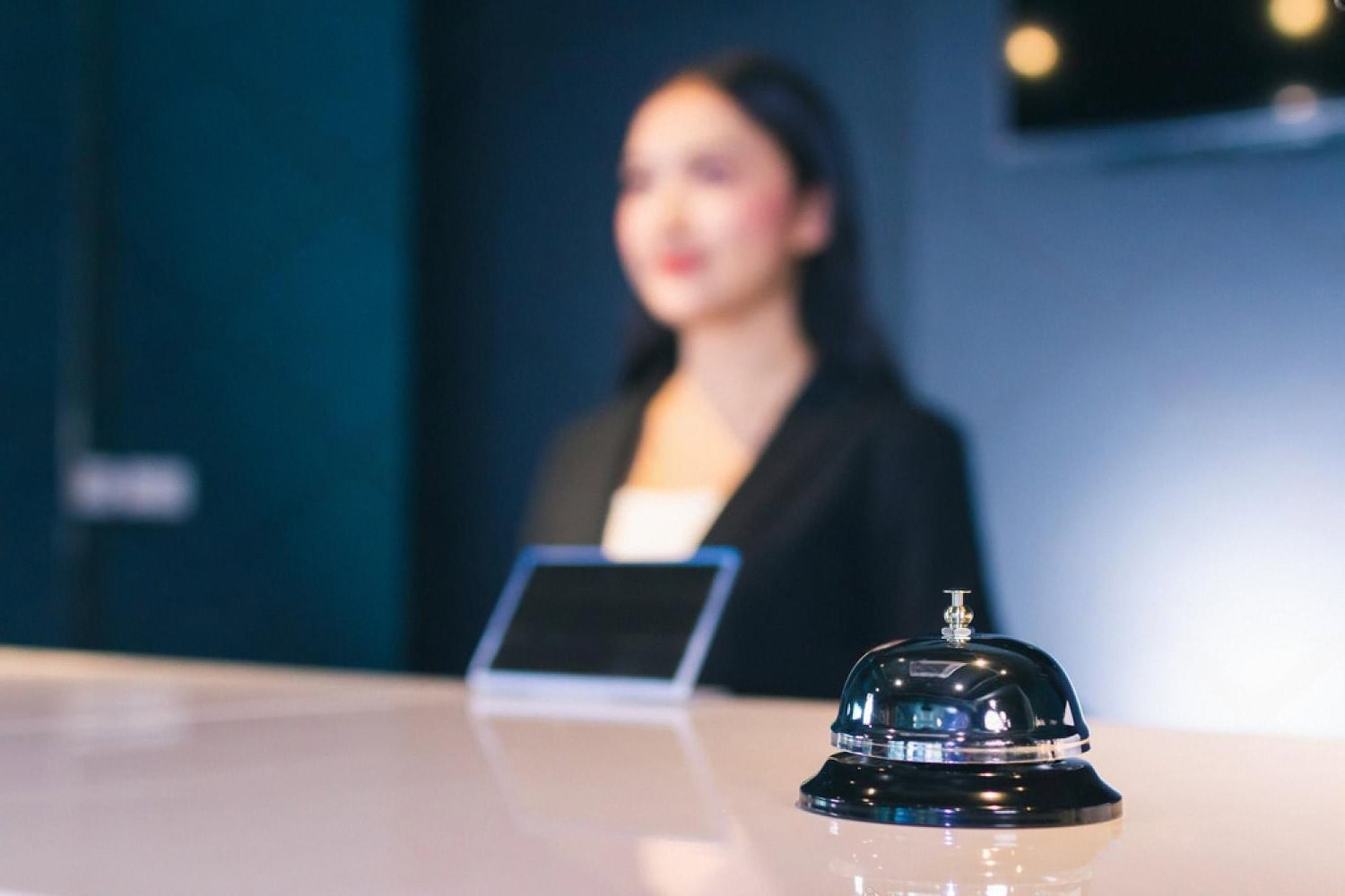 Hotel front desk with a service bell and a receptionist behind a self-service screen