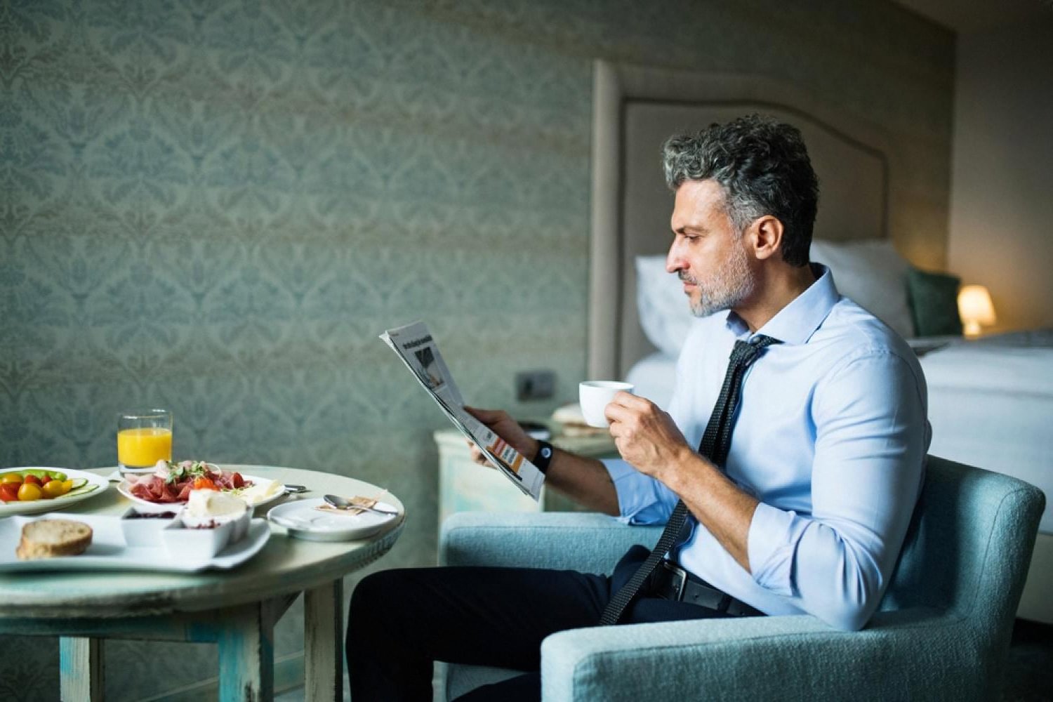 Business traveler in a US hotel room reading a newspaper over coffee and room service breakfast
