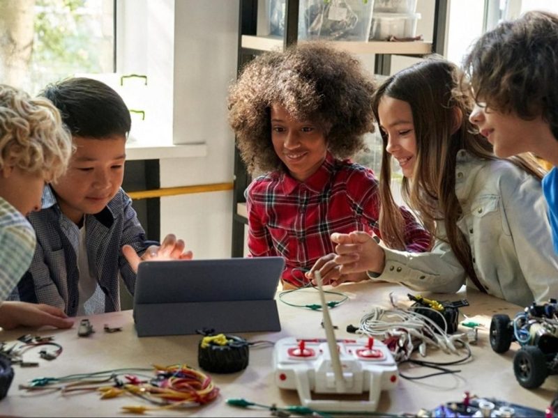Group of school students gathered around a tablet and robotics parts at a science exhibition workbench