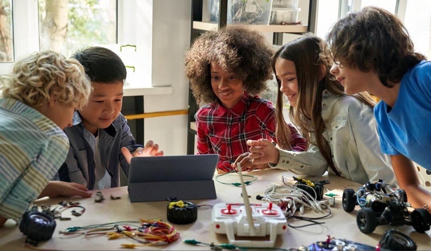 Group of school students gathered around a tablet and robotics parts at a science exhibition workbench
