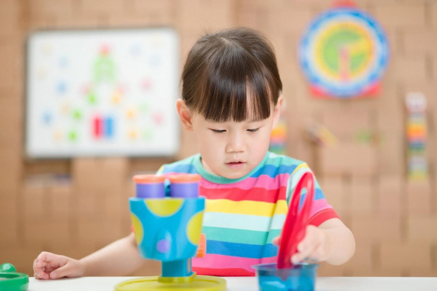 Young child in a colourful shirt experimenting with a small science kit at a classroom table