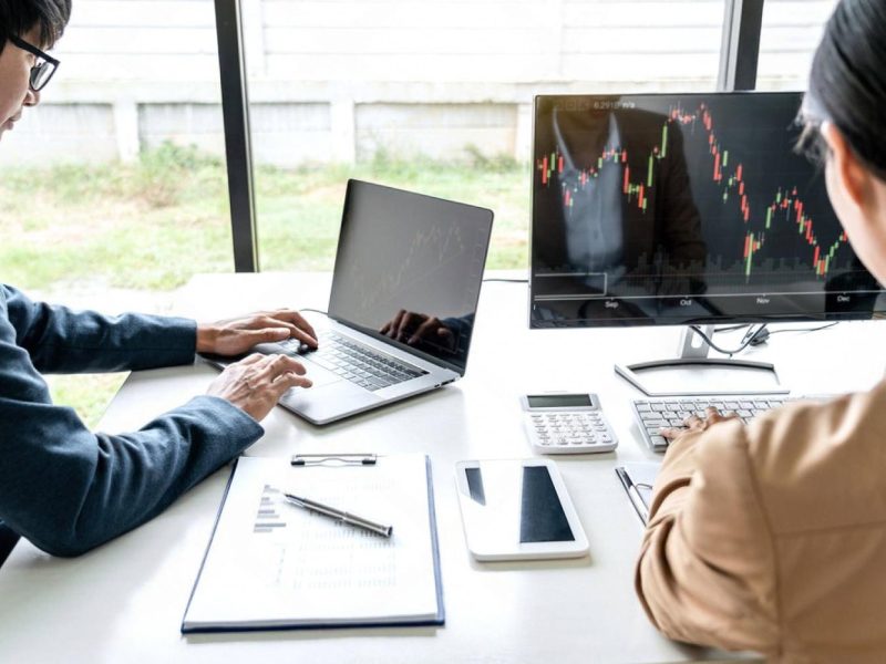 Traders analysing global market charts on a laptop and monitor while assessing trade risks