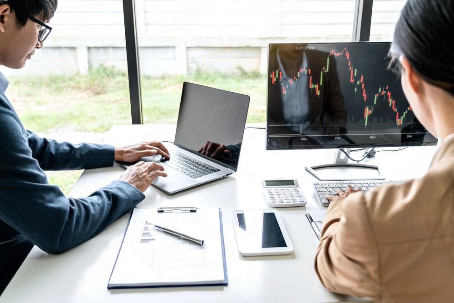 Traders analysing global market charts on a laptop and monitor while assessing trade risks
